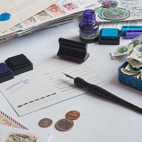 Postcrossing still life. Unwritten postcard in the center, ink bottle, fountain pen, stamps, coins around.